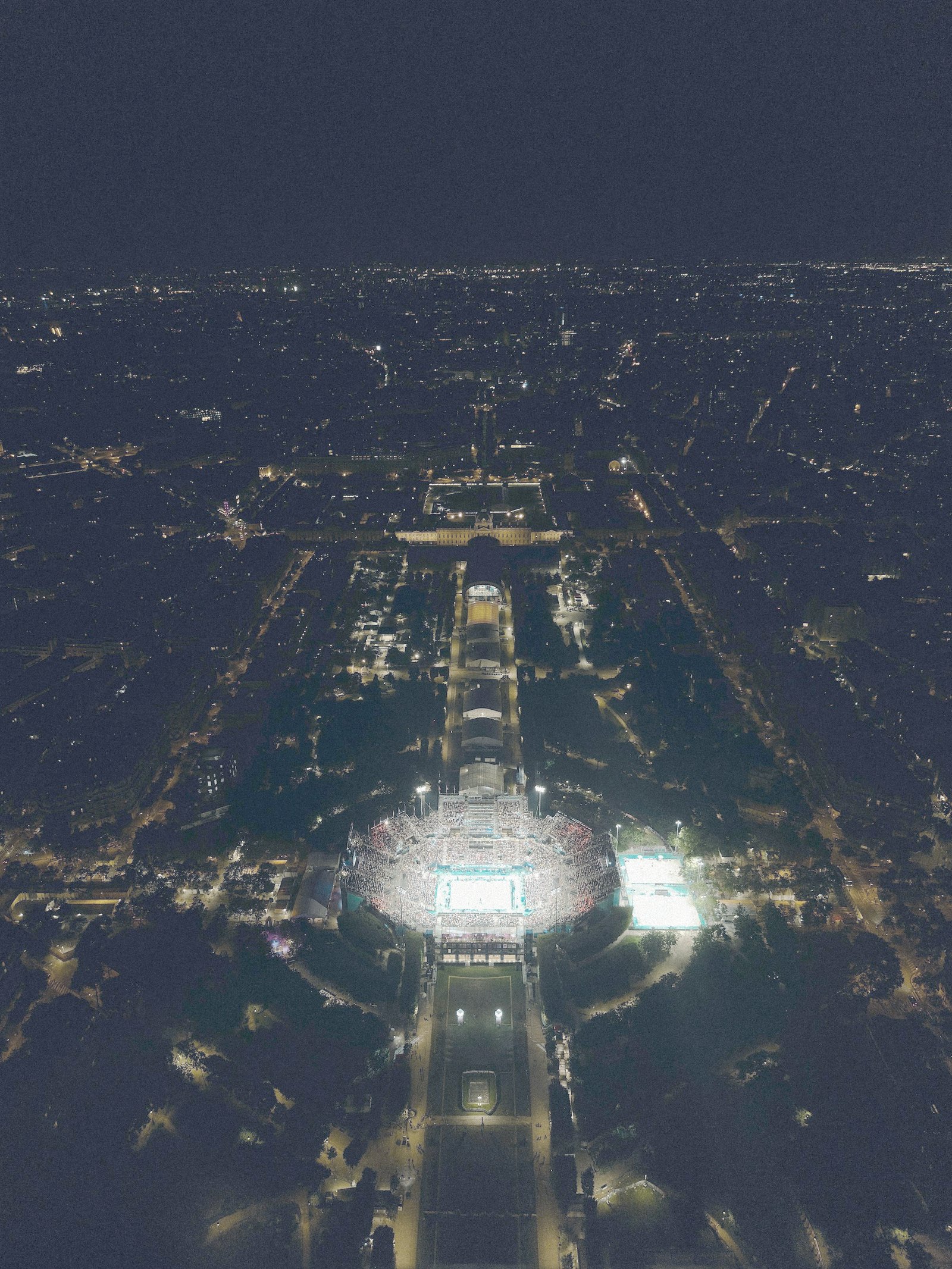 A long avenue at night leading to a lit stadium, seen from above