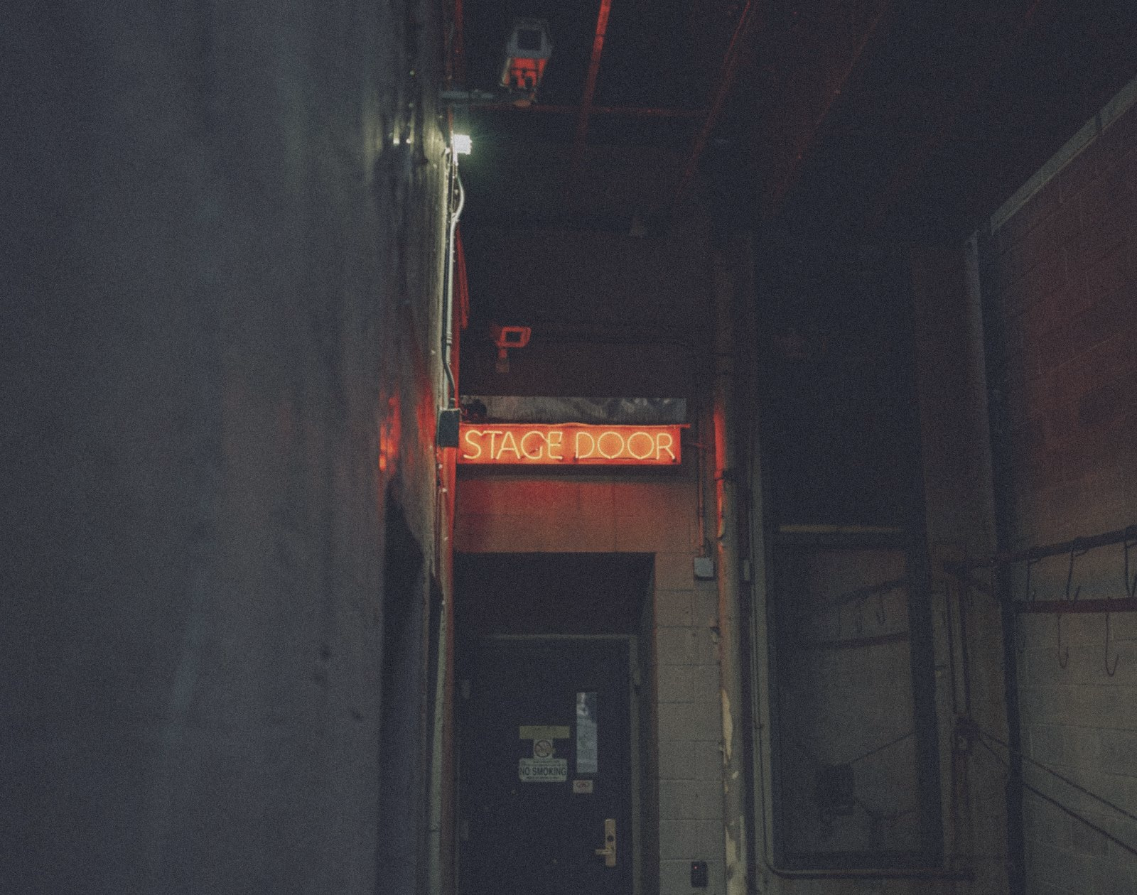 A red neon stage door sign in a dark passage