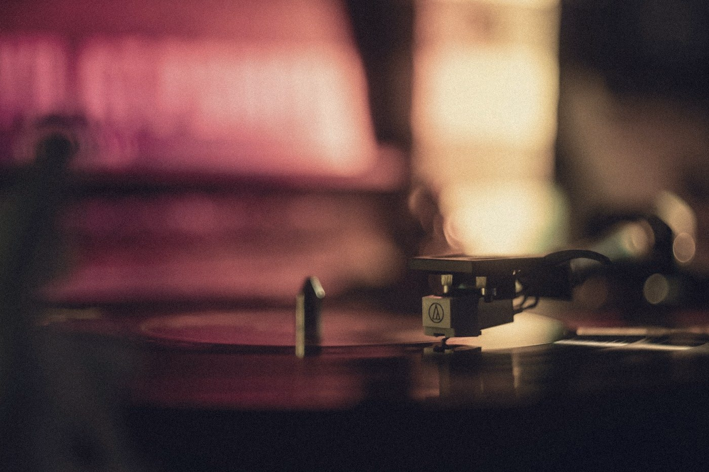 A turntable needle on a record in dusky pink light