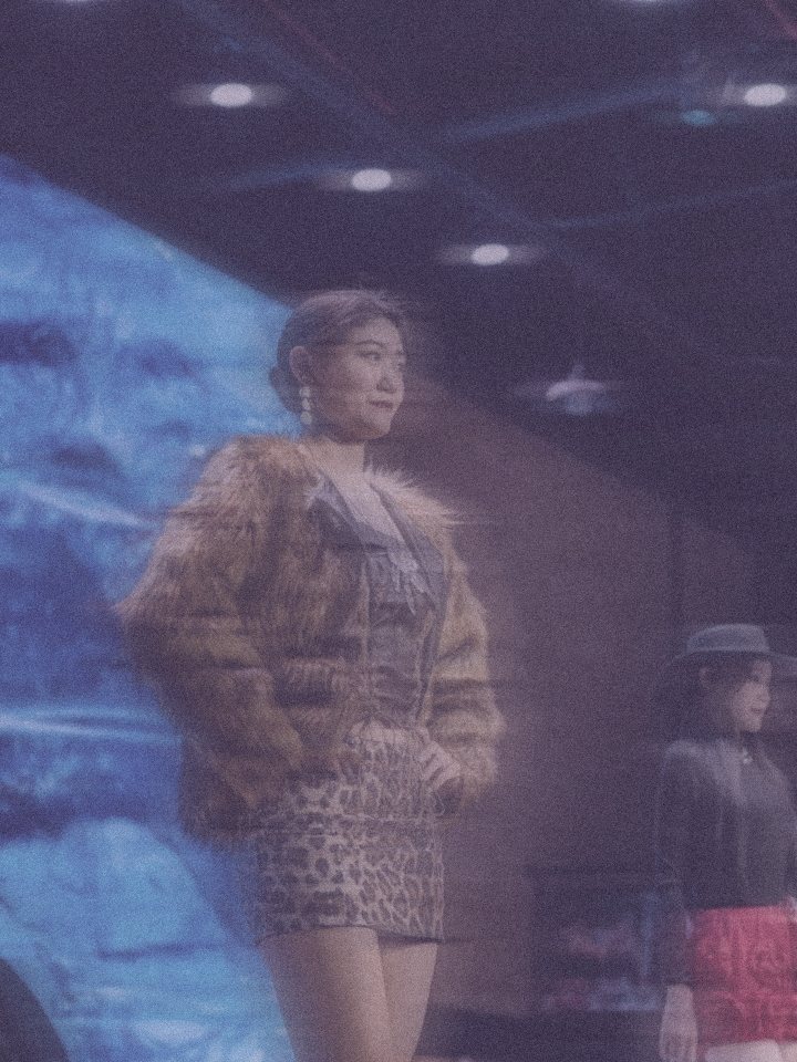 A model in a fur coat on stage, in lilac light